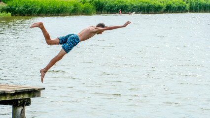 Teenagers jump into the water and swim in the lake on a hot summer day. Active recreation on an open pond. Children jump into the water and perform acrobatic tricks.