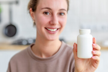 Happy young woman holding bottle of dietary supplements or vitamins in her hands. Close up. Healthy...
