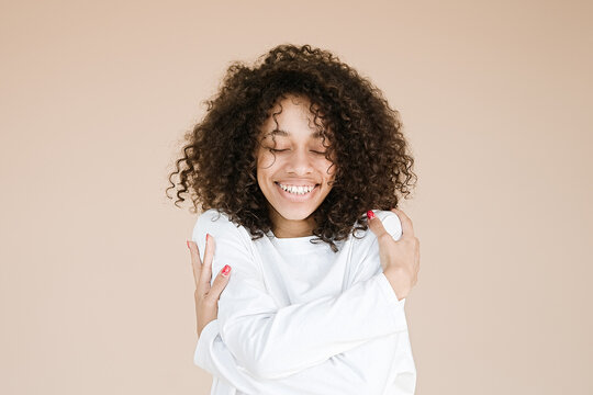 Photo of smiling african american girl with closed eyes holding hands on shoulders wear casual white t-shirt isolated beige background 