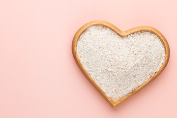Wheat flour in a wooden heart shape bowl on a pastel background.