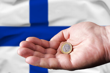 Obraz na płótnie Canvas Coin one euro in the hand of a man, the flag of Finland on the background