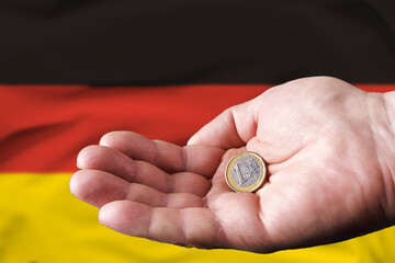 Plakat Coin one euro in the hand of a man, the flag of Germany on the background