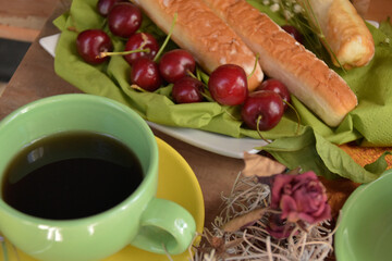 Tazas y tetera en mesa preparada para desayunar con pastas y cerezas