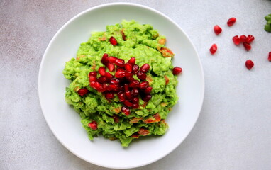 green pea guacamole with pomegranate seeds on a white plate of selective focus.