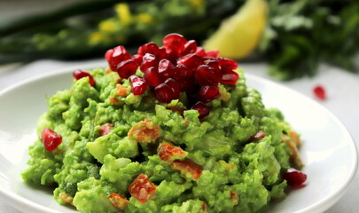 green pea guacamole with pomegranate seeds on a white plate of selective focus.