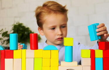 children's wooden geometric shapes multicolored close-up on the table and baby boy in the background with the process of playing selective and soft focus.