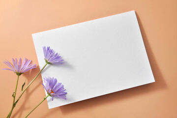 An empty white paper with a place for writing on a beige background and flowers next to it. 