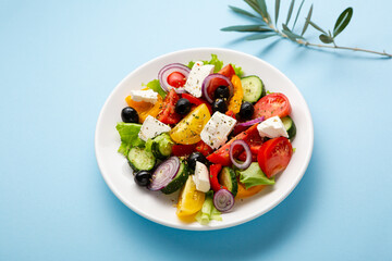 Overhead view of Greek salad on plate on blue surface healthy food