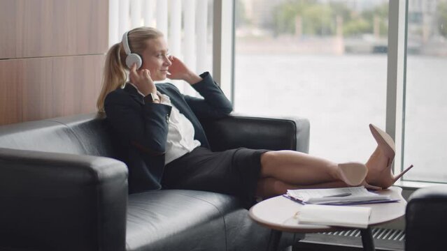 Businesswoman in headphone relax on sofa in office lobby. Realtime