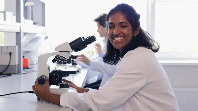 science research, work and people concept - female scientist with microscope working in laboratory