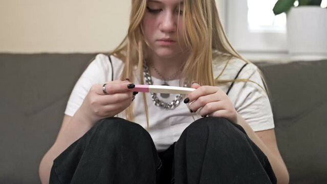 Teenage girl looks at the result of a pregnancy test and cries. The social problem.
