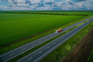 red cargo truck on the highway. asphalt road among green fields and beautiful clouds. cargo delivery and transportation concept