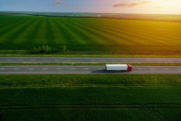 red cargo truck on the highway. asphalt road among green fields at sunset. cargo delivery and transportation concept