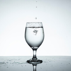 Glass cup filled with water with falling drops.