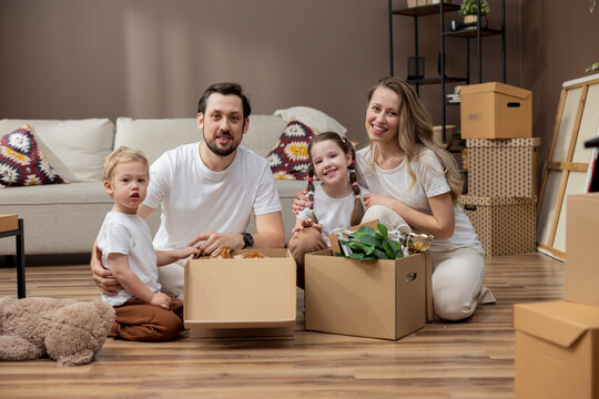 Portrait of a young family with children moving into a new home. Cooperation in unpacking boxes.