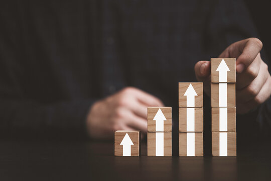 Hand putting up arrow which print screen on wooden cube block for business and sale growth concept.