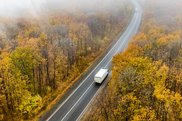 white van on the asphalt road through the autumn forest into the mist. cargo delivery and transportation concept. fog on the road