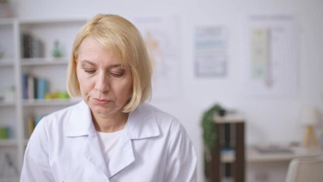 Confused female doctor writing symptoms in patient's medical record, diagnostics