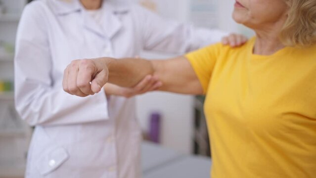Rehabilitation center employee examining senior patient's arm after sprain