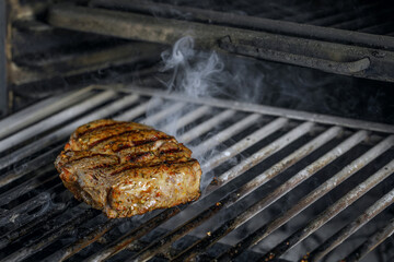 roasted meat beef steak  grilling on rack charcoal stove with smoke on black background.