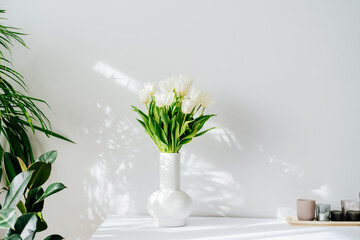 Scandinavian home interior with spring bouquet of white tulip flowers in ceramic vase standing on...