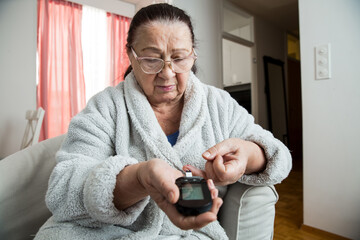 Senior woman checking blood sugar level using home glucometer. Old person with diabetes at home in...