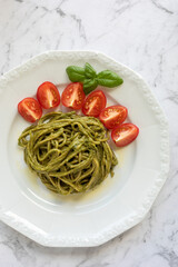 Spaghetti with pesto made of mustard greens, basil and walnuts, tomatoes and basil spring. Top view.
