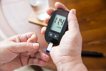 Senior woman checking blood sugar level using home glucometer. Close-up hand of old person with...