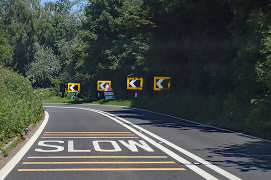 Black and white chevrons, a double white line and a skid risk warning sign tell drivers to slow down because there is danger ahead around the curve