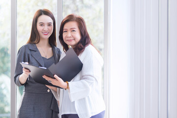 Professional Asian female talks with her woman boss to consult about work in file document in her hands at workplace.