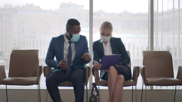 Job applicants in face mask sit in office hall and discuss application. Realtime
