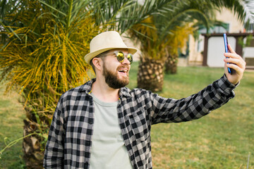 Obraz premium Man taking selfie portrait over palm tree background - Happy millennial guy enjoying summer holidays in city - Youth and technologies