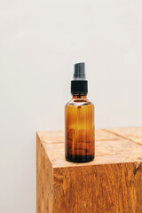 Glass amber natural oil or serum bottle and wooden stool against gray bathroom background with copy space. Eco friendly sustainable zero waste cosmetic product for skin care.