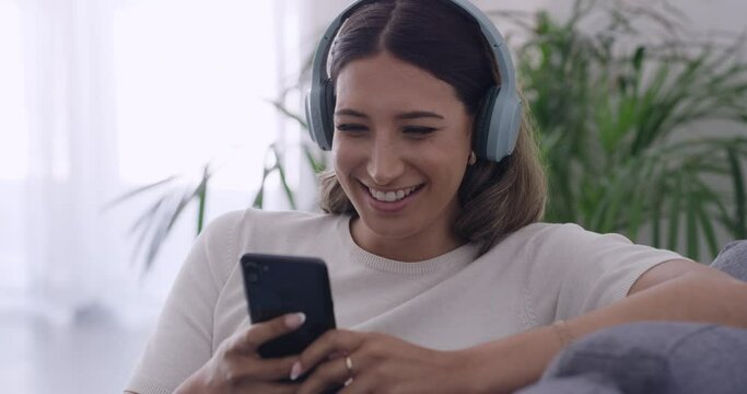 Woman laughing watching funny videos online with her phone at home. Female streaming series and chatting with friends on social media. Girl smiling while sending text message and listening to podcast