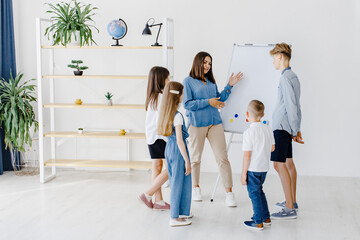 Fototapeta premium Explaining lesson and using board. Group of children students of different ages in class at school with teacher. Learning concept