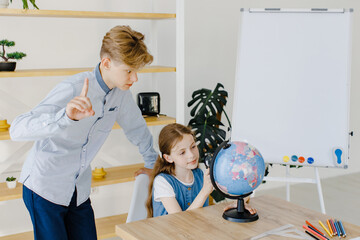 Teenage girl and boy siting near table with globe in classroom. Teen schoolboy and schoolgirl doing project together at school. Conception of education.