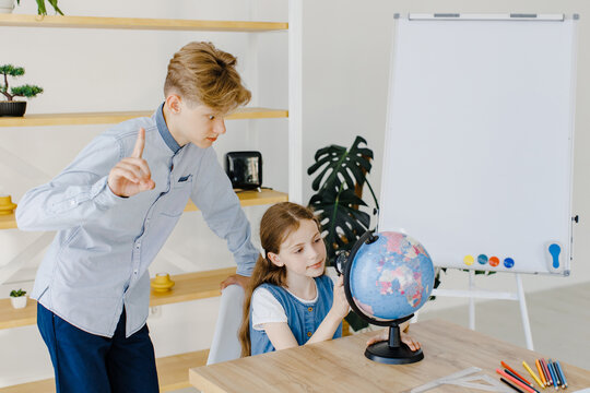 Teenage girl and boy siting near table with globe in classroom. Teen schoolboy and schoolgirl doing project together at school. Conception of education. - Powered by Adobe