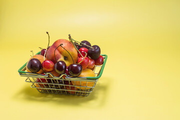 A full basket of fresh fruits bananas, cherries, nectarine, apricots, peaches on a bright yellow background of the copy space.
