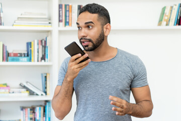 Hispanic hipster man with beard sending voice meassage at mobile phone
