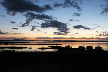 Landscape dark silhouettes of cars on the background of a pond with the rays of the setting sun. Tourists on vacation.