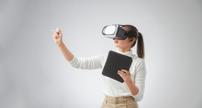 Woman in VR glasses. Business young woman in virtual reality headset pointing in the air while using tablet on her working area. - Powered by Adobe