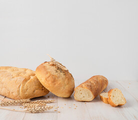 Fresh white wheat bread, round classic, ciabatta, french baguette, wheat ears and grains on white wooden background. Bread making, bakery, healthy food. Bread background. Light mockup