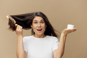 beautiful cute attractive middle-aged brunette combing her long hair with a wooden comb while...