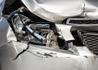 The front part of the silver car is damaged as a result of an accident on the road. The front part of the car is silver, damaged and broken as a result of an accident. Hood, headlight, bumper. 