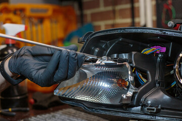 Car headlight in repair close-up. The car mechanic installs the lens in the headlight housing. The...
