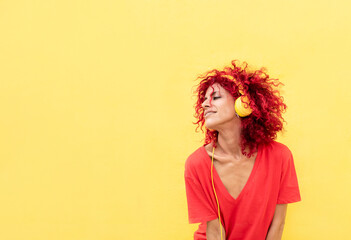 cheerfull mid adult latin woman with afro red hair and yellow headphones over yellow background wearing red shirt