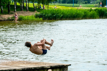 Teenagers jump into the water and swim in the lake on a hot summer day. Active recreation on an open pond. Children jump into the water and perform various acrobatic tricks.