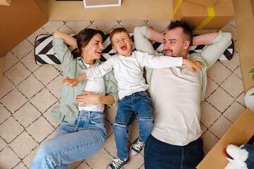 Happy family lying on the floor in new home with cordboard boxes around