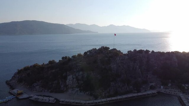 Rock in sea bay with sand beach and turkish flag on top in small touristic village Turunc. Landscape with moored pleasure yacht. Drone view
