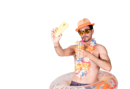 Portrait of a young smiling tourist with a flower necklace, hat and sunglasses wearing an inflatable float drinking his cocktail while taking a selfie photo.